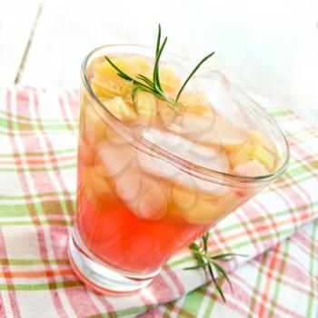 Lemonade with rhubarb and rosemary in a glass on a napkin on a wooden boards background