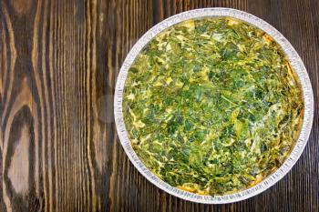 Celtic cake with spinach, tomatoes, oatmeal and eggs in baking dish from a foil against the backdrop of wooden planks on top