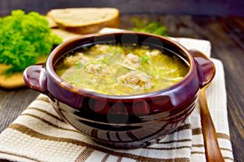 Soup with meatballs, noodles and vegetables in a clay bowl, spoon on a napkin, parsley, bread on a wooden boards background