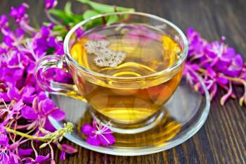 Herbal tea in a glass cup, fresh flowers fireweed against the dark wooden board