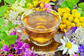Herbal tea in a glass cup from fresh flowers fireweed, tansy, chamomile, clover, yarrow, meadowsweet, mint leaves on a dark wooden board