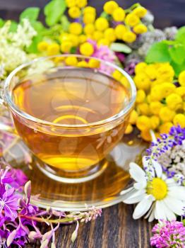 Herbal tea in a glass cup from fresh flowers fireweed, tansy, chamomile, clover, yarrow, meadowsweet, mint leaves on a wooden boards background