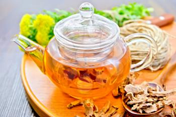 Herbal tea in a glass teapot from the root of Rhodiola rosea on a round tray, fresh flowers and dried root of Rhodiola rosea on the background of wooden boards