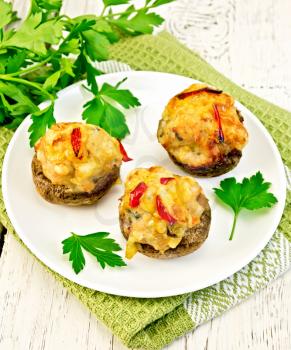 Mushrooms stuffed with meat with parsley and tomatoes in a white plate on a green kitchen towel, fork on the background of wooden boards