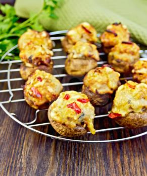 Mushrooms stuffed with meat and pepper on a metal grid, green tea towel, parsley on a wooden boards background