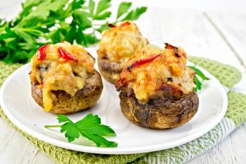 Mushrooms stuffed with meat with parsley and tomatoes in a white plate on a green napkin and fork on a wooden boards background