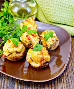 Mushrooms stuffed with meat with parsley and pepper in a brown plate green towel on a wooden boards background