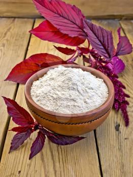 Amaranth flour in a clay bowl and purple amaranth flower on the background of wooden boards