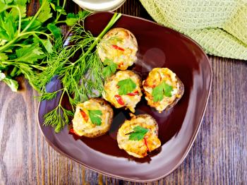 Mushrooms stuffed with meat with parsley and pepper in a brown plate green kitchen towel on the background of the wooden planks on top
