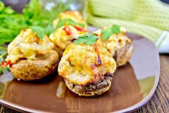 Mushrooms stuffed with meat with parsley in a brown plate green kitchen towel on the background of wooden boards