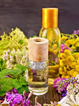 Oil and lotion bottles, fireweed flowers, tansy, chamomile, clover, yarrow and meadowsweet, mint leaves on a dark wooden board