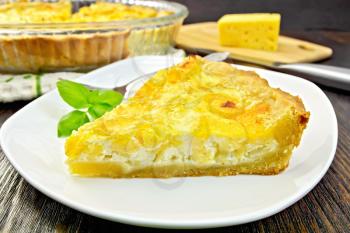 Tart with cheese, leek and sour cream and egg cream in a dish, cheese and knife on a wooden boards background