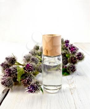 One vial of oil with flowers and leaves of burdock on a wooden boards background
