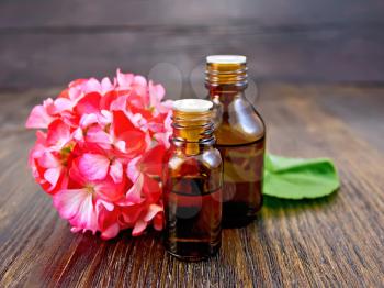 Two bottle of oil with green leaf and flower of pink geranium on a wooden boards background