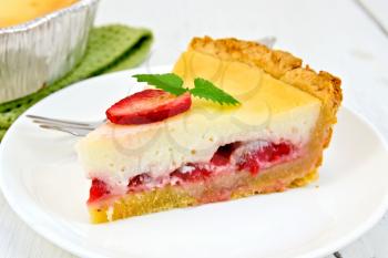 A piece of strawberry pie with cream sauce, fork, strawberry, mint in white plate, napkin and shape with a pie on the background light wooden boards