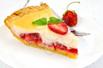 A piece of strawberry pie with cream sauce, fork, strawberry, mint in a bowl on the background light wooden boards