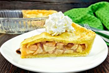 Classic American apple pie with whipped cream in a plate, napkin on a wooden boards background