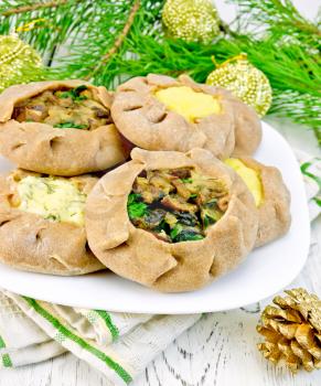 Carols of rye flour filled with cheese, potatoes and mushrooms on a plate, napkin, Christmas decorations, tree branches on the background of wooden boards