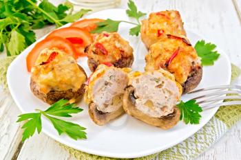 Mushrooms stuffed with meat whole and sliced parsley and tomatoes in a white plate on a napkin, fork on the background of wooden boards