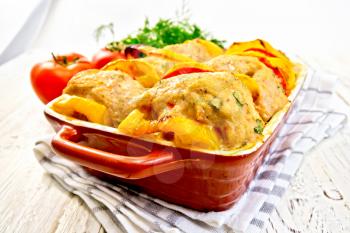 Cutlets of turkey meat baked with red tomatoes and yellow pepper in a ceramic roasting pan on a towel, parsley on a wooden boards background