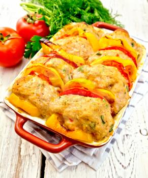 Cutlets of turkey meat baked with tomatoes and yellow pepper in a ceramic roasting pan on a towel, parsley on the background light wooden boards