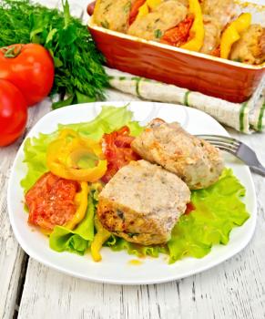 Cutlet of turkey meat with lettuce, tomato and pepper in a bowl, parsley, towel and plug roaster with cutlets on a wooden boards background