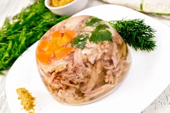 Jellied pork and beef with carrots and parsley on a plate with mustard and dill, a towel on the background light wooden boards