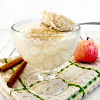 Air apple jelly in a glass bowl with a spoon, red apples and cinnamon on a towel on the background light wooden boards