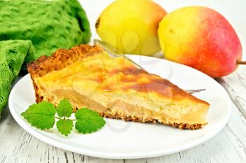 One slice of pear cake with cream sauce in white plate, fork, pear and mint, napkin on a wooden boards background