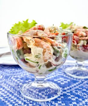 Salad with shrimp, avocado, tomatoes, green lettuce in a glass goblet, a plate against the background of a linen tablecloth