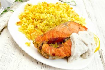 Pink salmon with lemon, milk sauce and rice with turmeric in a dish, kitchen towel and fork on a background of wooden light boards