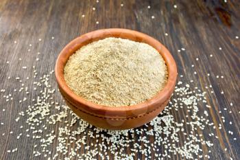 Sesame flour in a clay bowl and sesame seeds on a wooden boards background