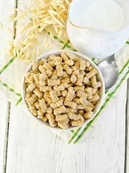Oat bran large in bowl, a jug of milk, oat stalks on a kitchen towel on the background of the wooden planks on top