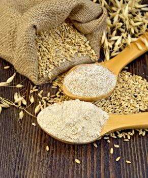 Flour and oat bran in two spoons, bag with oat and stalks of oats on the background of wooden boards