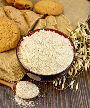 Oat flour in a bowl, bag with oat and stalks of oats, biscuits and bread, oatmeal on the background of wooden boards