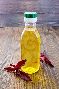 One plastic bottle of oil with a branch burgundy amaranth on a dark wooden board