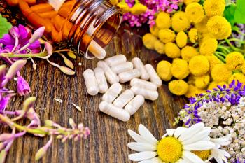 Capsules in brown jar open and on table, fresh flowers fireweed, tansy, chamomile, clover, yarrow, meadowsweet, mint leaves on dark wooden board