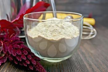 Amaranth flour in a glass cup with a mixer, purple amaranth flower on a background of wooden boards