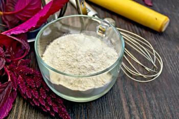 Amaranth flour in a glass cup with a mixer, a rolling pin and sieve, purple amaranth flower on a background of wooden boards
