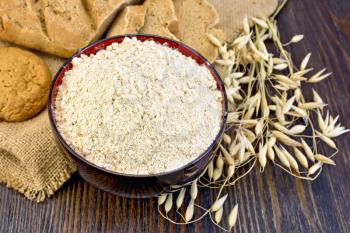Oat flour in a bowl, cookies and bread made from oatmeal on sackcloth, stalks of oats on the background of wooden boards