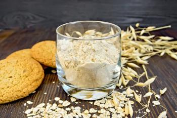 Flour oat in a glassful, oatmeal and ears, cookies on a background of wooden boards