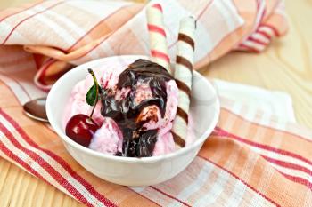 Ice cream cherry in a bowl, chocolate syrup and wafer rolls on a napkin against the background of wooden boards