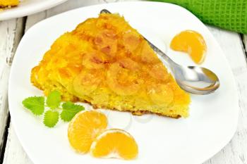 Tart with mandarin, mint, tangerine slices and spoon in white plate, towel on a background of wooden boards