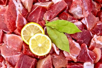 Texture of pieces of raw meat with bay leaves and lemon wedges