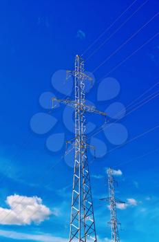 A number of pylons high-voltage power lines against the blue sky and white clouds