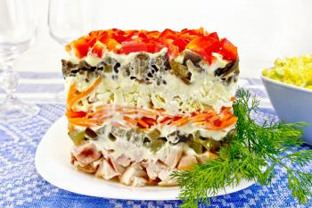 Layered salad with chicken, egg, mushrooms and cucumber, carrots and pepper, mayonnaise on the plate with dill on the background of the tablecloth