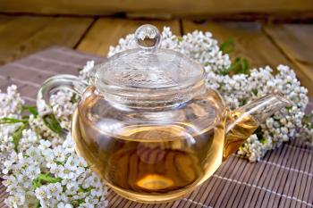 Tea with yarrow in a glass teapot, fresh flowers, yarrow on background of bamboo towels and wooden boards