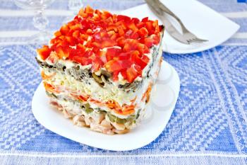 Layered salad with chicken, egg, mushrooms and cucumber, carrots and pepper, mayonnaise in a dish on the background of the tablecloth