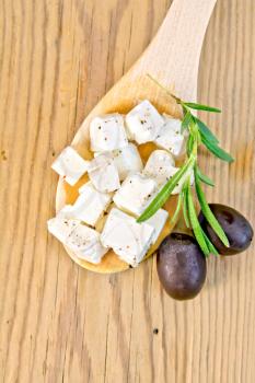 Feta cheese with spices in spoon, olives and rosemary on background wooden board