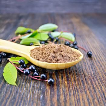 Flour of bird-cherry in a spoon with berries on a background of dark wooden boards